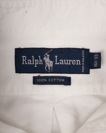 Close-up of a white Ralph Lauren garment showing the navy blue brand label with the white polo player logo and text, plus a smaller '100% COTTON' tag below.
