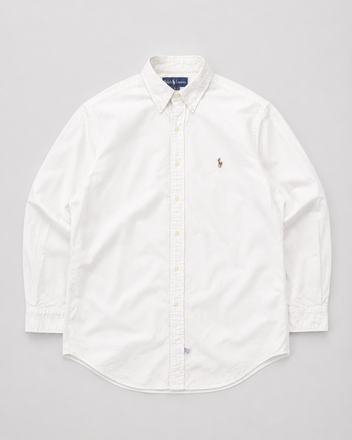 A white long-sleeve button-down shirt by Polo Ralph Lauren, featuring the signature embroidered polo player logo on the left chest, laid flat against a light gray background.