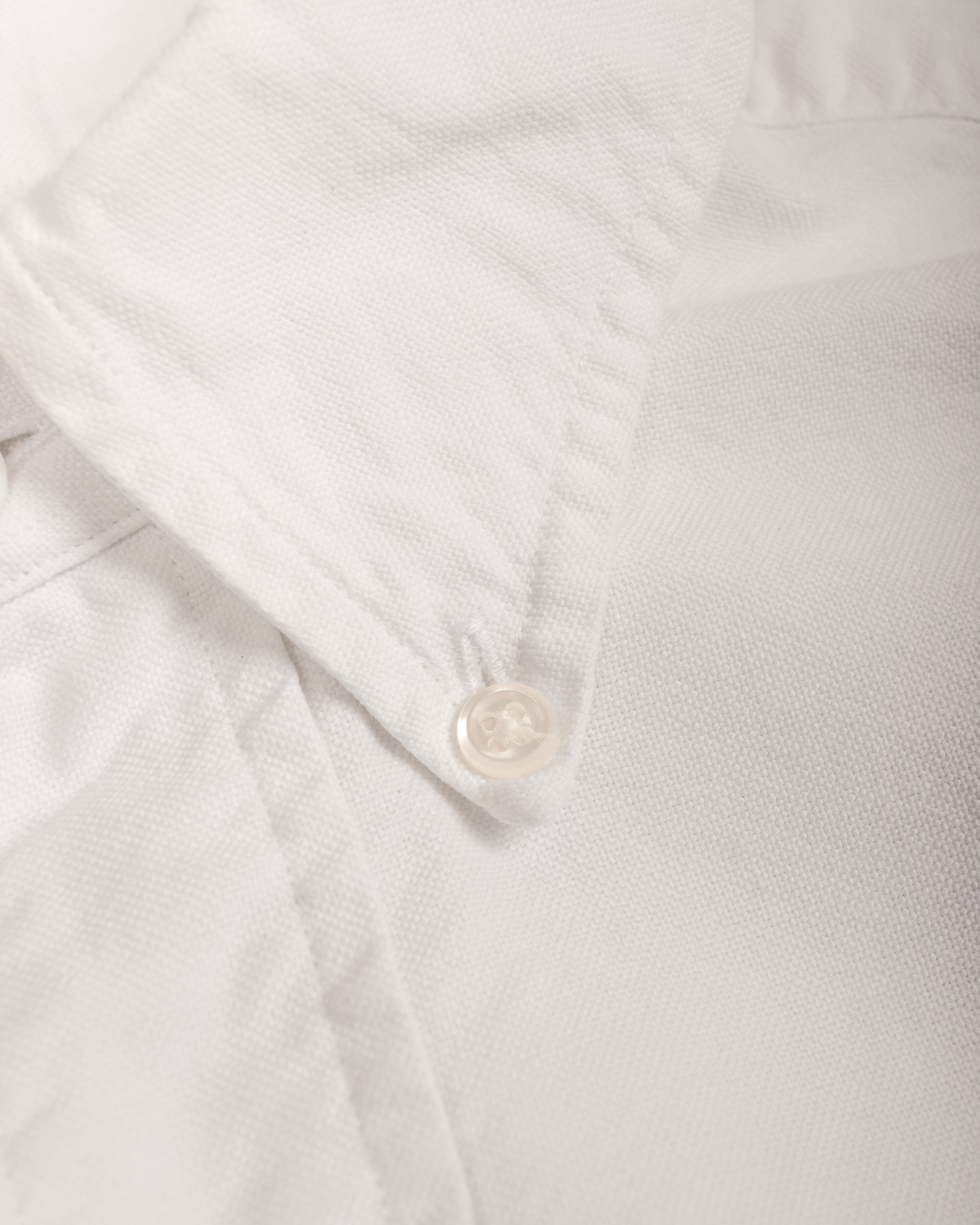 Close-up of a white textured button-down shirt collar with a single white button.