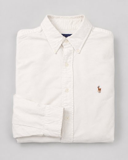 A folded white long-sleeve button-down shirt with a small embroidered polo player logo on the left chest, set against a neutral gray background.