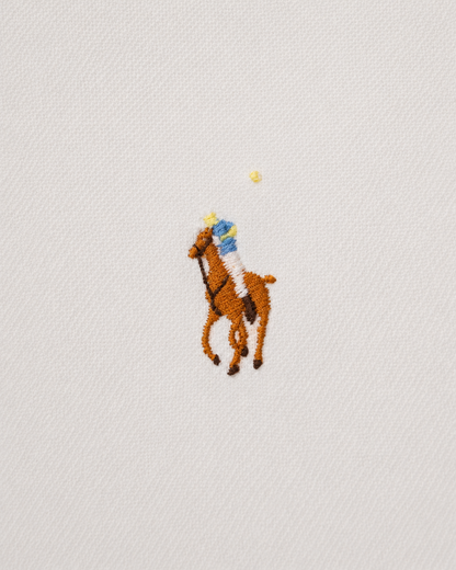 A close-up of a white textured fabric featuring the embroidered polo player logo on the chest, with a small yellow star above the horse.