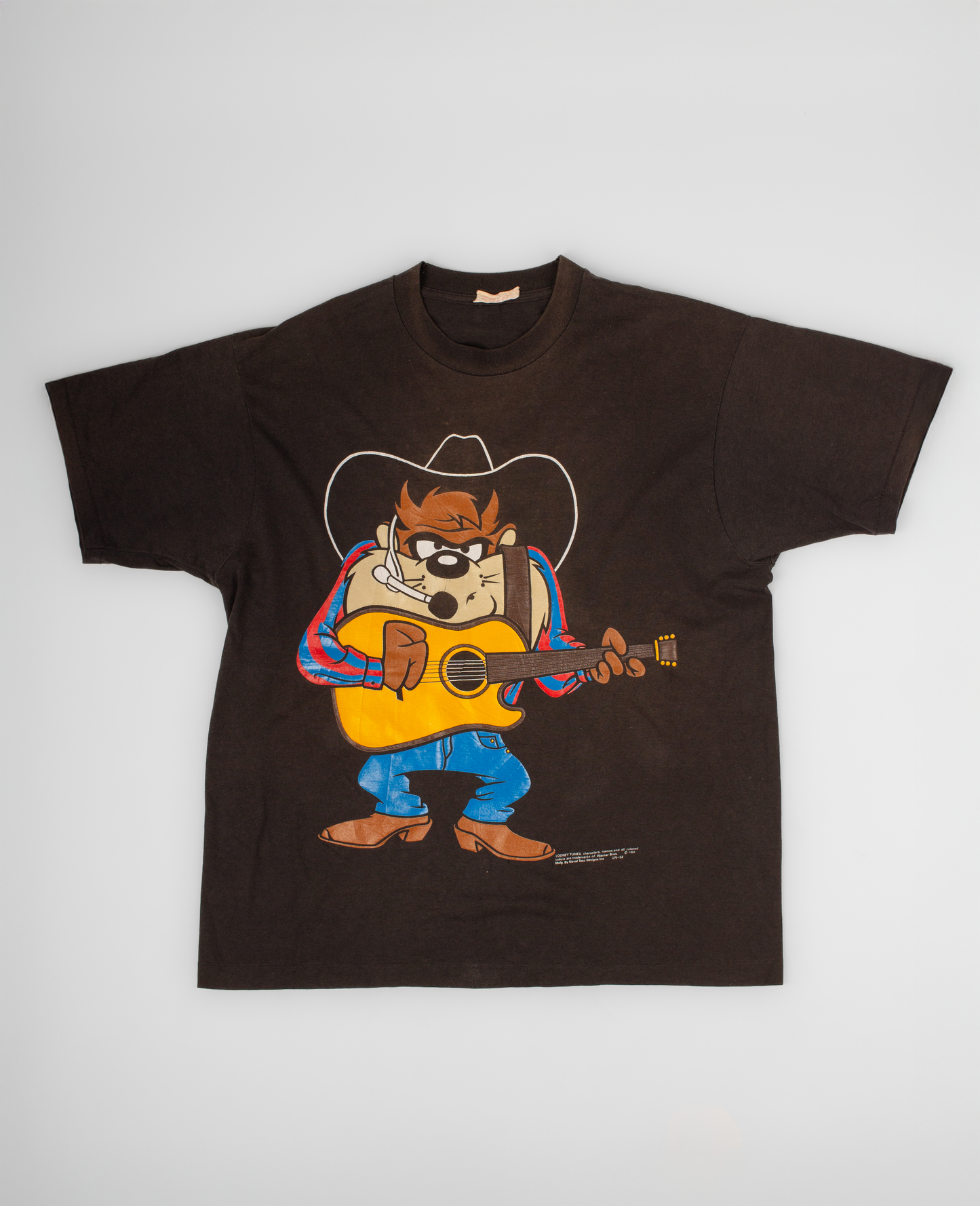 Brown t-shirt with cartoon character playing guitar on a white background Vintage Taz Tasmanian Devil tee featuring the beloved Looney Tunes character dressed as a country musician. During the 1990s, character graphic tees became a staple of American pop culture, with Taz standing out as one of the era’s most recognizable and collectible cartoon icons. A fun piece that blends vintage animation nostalgia with classic Americana style. single stitch

100% cotton, 1993, single stitched, made in USA, good fade